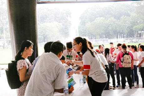 People standing in line at a community event table, representing traditional fundraising and community engagement activities.