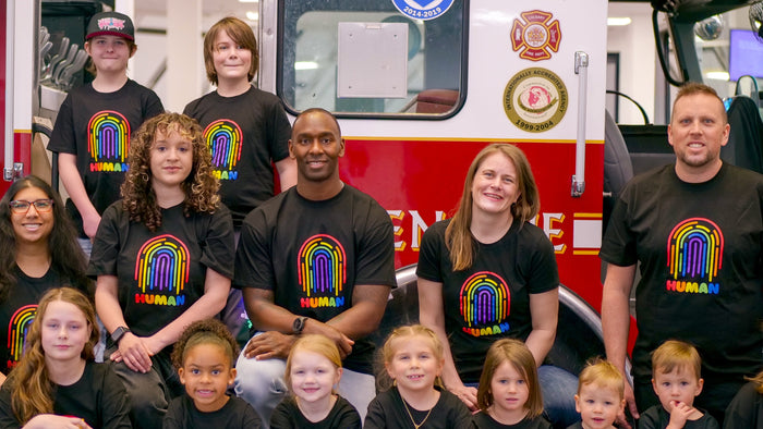 Group of people, including children and adults, posing in front of a fire truck wearing a pride tshirt.